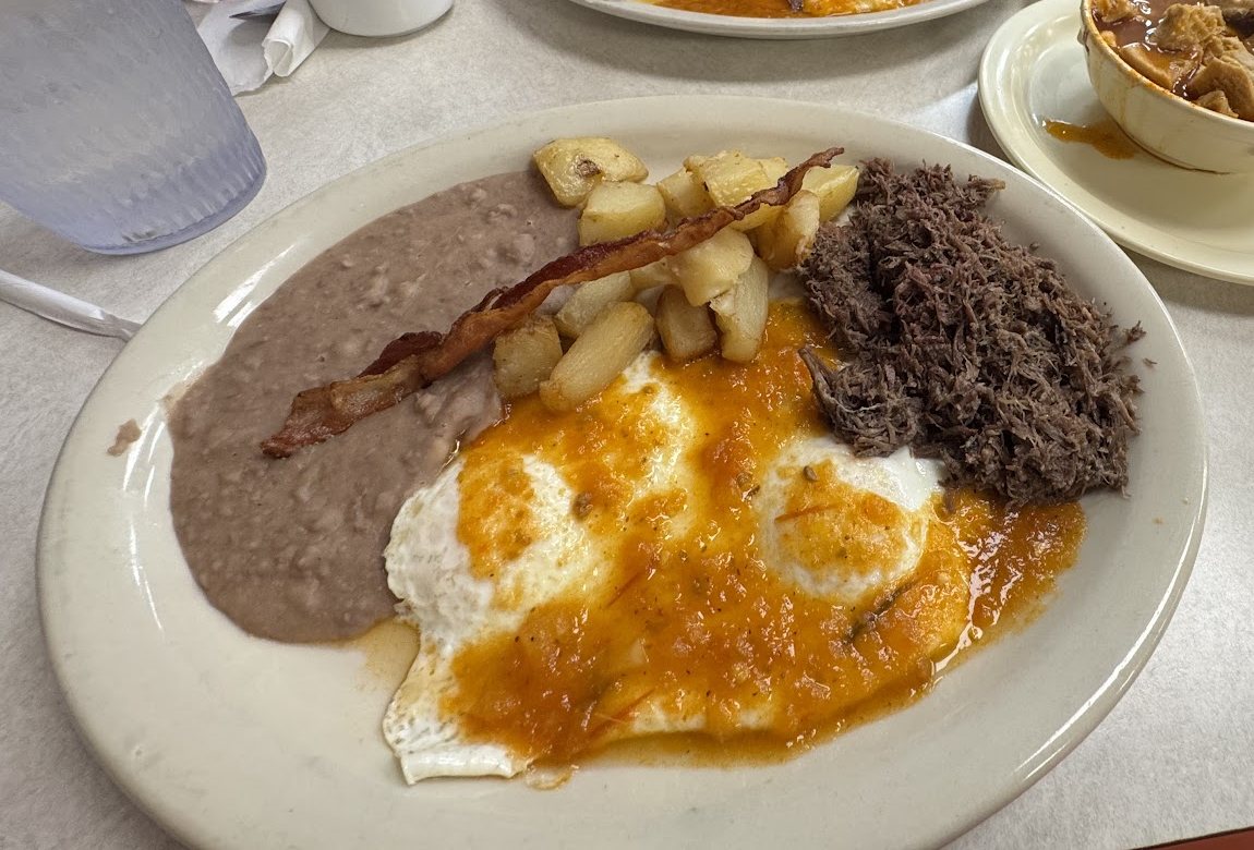 Breakfast plate of eggs in ranchero sauce with barbacoa, bacon, potatoes and refried beans