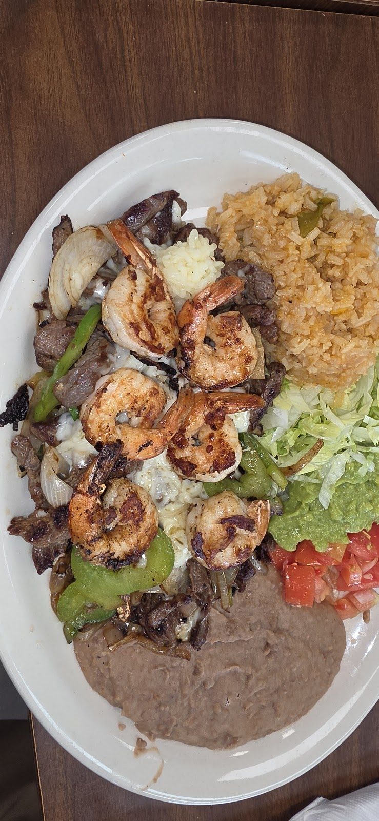 Plate of beef fajitas topped with grilled shrimp, rice, beans and salad