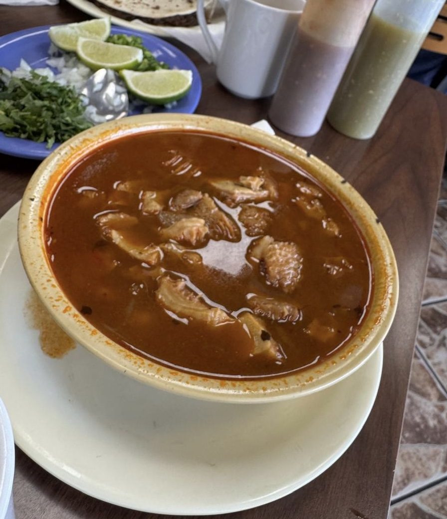 Bowl of red menudo with lime, cilantro and onion on the side